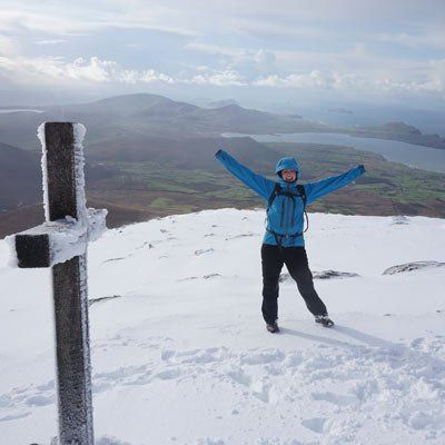 a happy climber at the cross on  mount brandon summit  in snow 