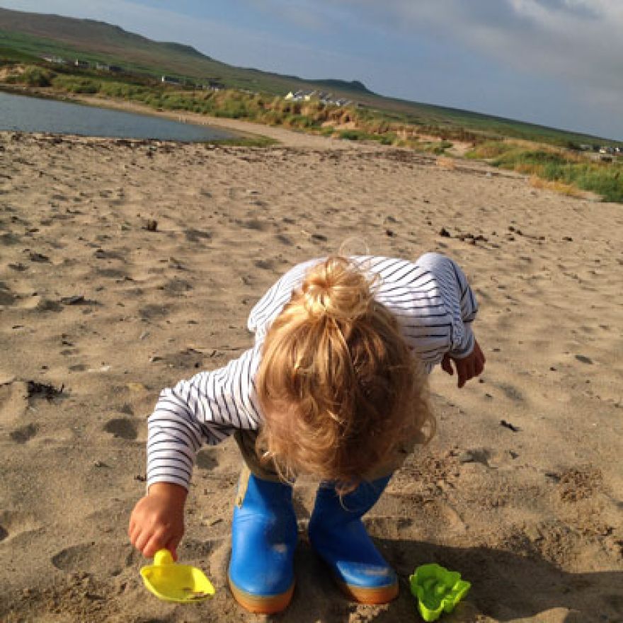 child holding a toy shovel playing on a sandy beach dingle peninsula Ireland