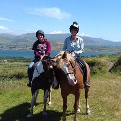two young girls sitting on horseback with Dingle harbour and mountains behind them