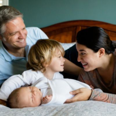 father mother toddler and baby on bed smiling